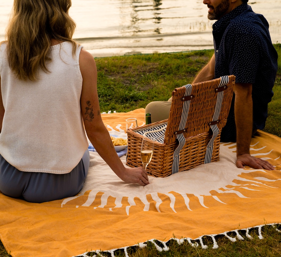 couple laying on blanket in front of water with picnic basket